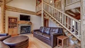 Un salon spacieux avec un canapé en cuir, une cheminée, des poutres apparentes et un escalier en bois.