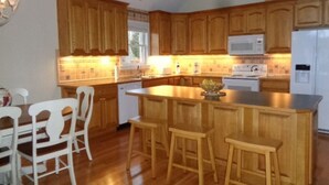 A kitchen with wooden cabinets, a central island with stools, a microwave, and a refrigerator.