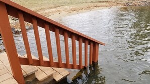 A wooden deck with a railing leading to a pond.