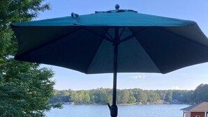 A wooden deck with a table and chairs, an umbrella, and a view of a lake and trees.