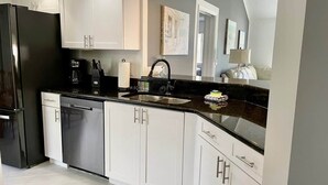 A modern kitchen with white cabinets, a black countertop, stainless steel appliances, and a sink.