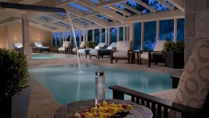 Ein Poolbereich mit Liegestühlen und einem Tisch mit Obst, unter einer überdachten Pergola mit großen Fenstern.