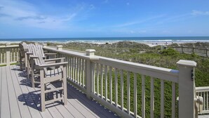 A wooden deck with white railings overlooking a beach.