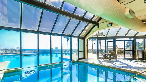 A large indoor swimming pool with clear glass walls and a view of the beach.