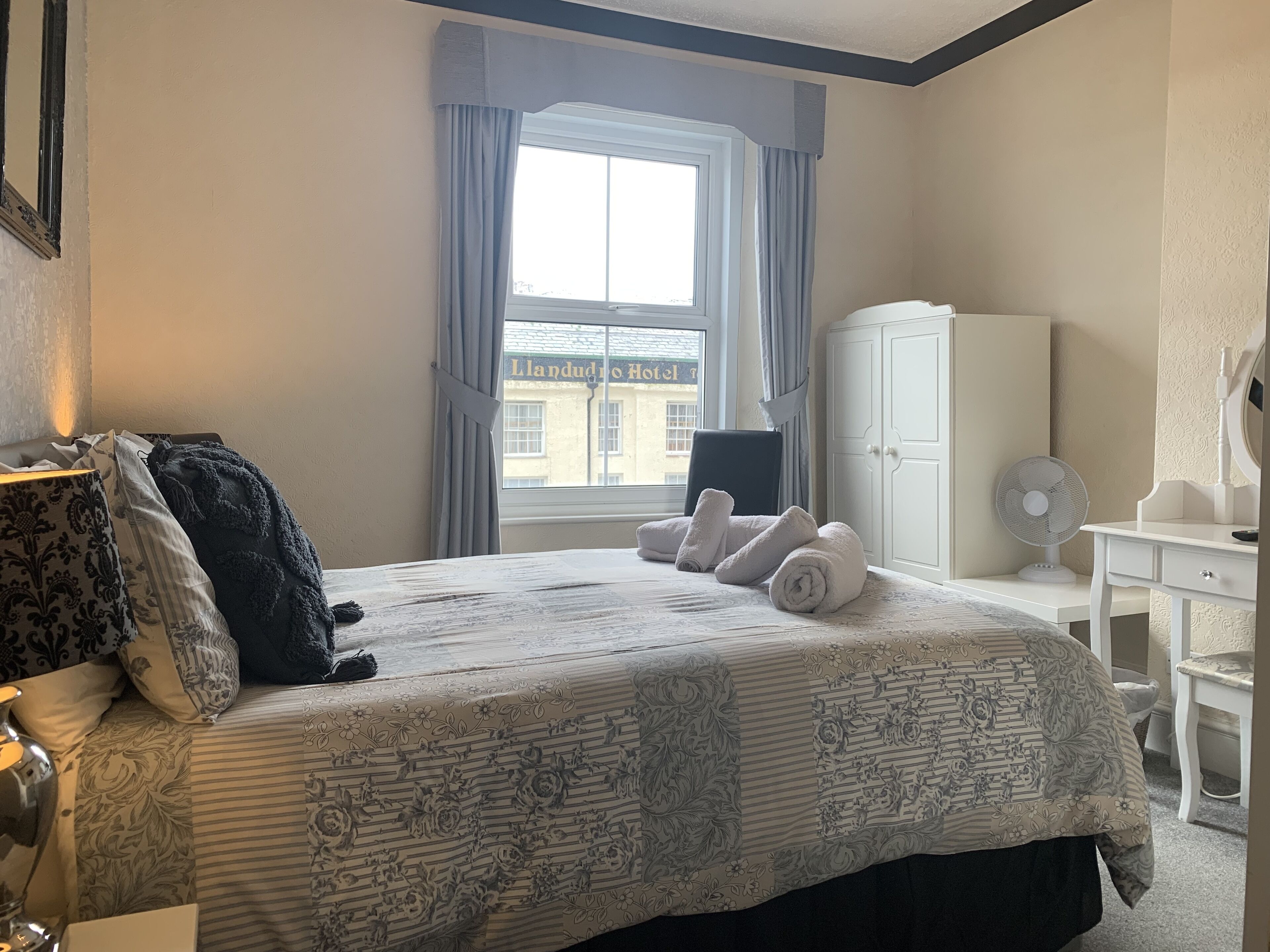 Una habitación de hotel con cama, armario, escritorio con lámpara y ventana con cortinas.