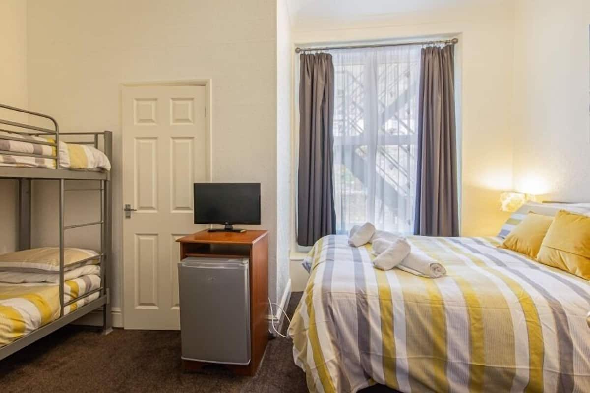 A room with bunk beds, a television, a small refrigerator, and a bed with striped bedding.