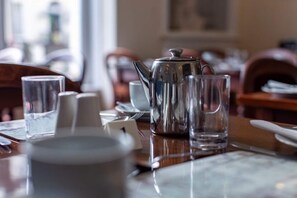 A dining table with a silver teapot, clear glasses, and a white cup. - The Capri Guesthouse (Llandudno)