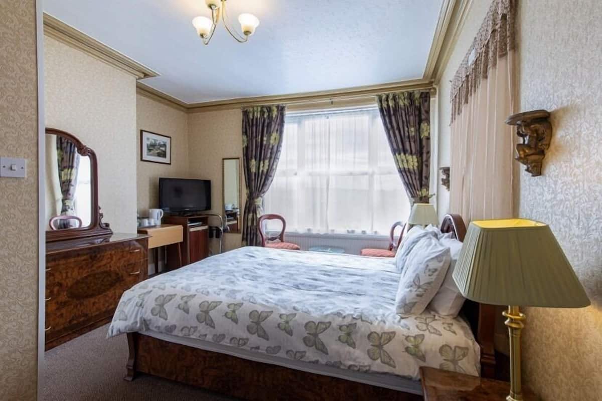 A hotel room with a bed, a desk, a television, and a lamp.