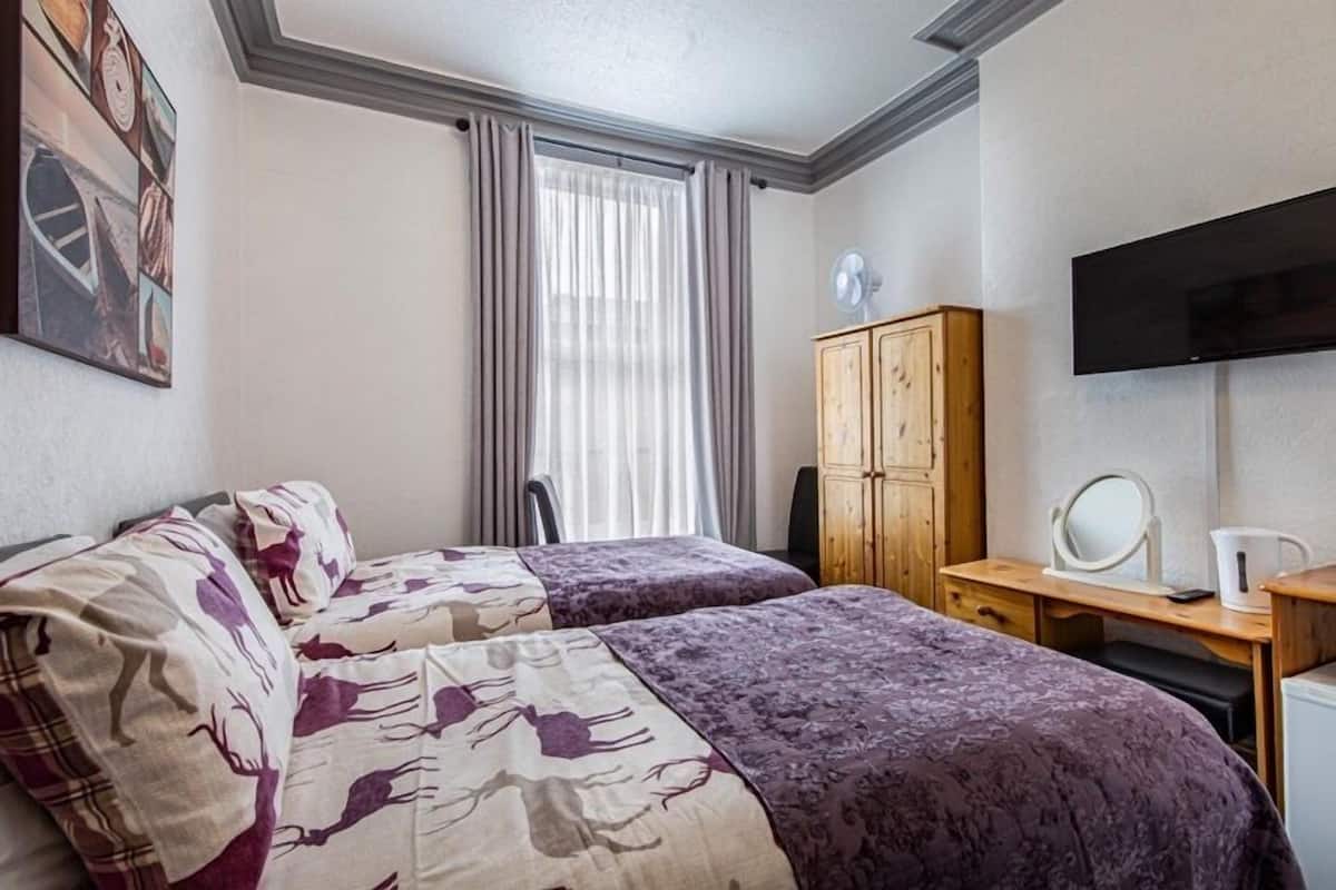 A hotel room with two beds, a wooden wardrobe, a desk with a mirror, and a television.