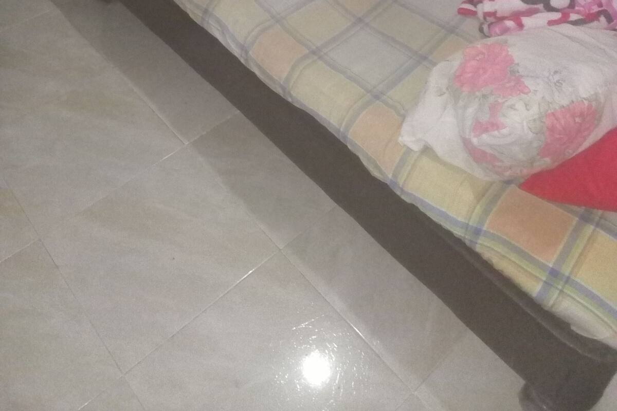 A small, dimly lit room with a single bed, a brick wall, and a tiled floor.