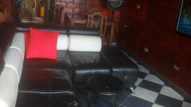 A living room with a black leather sofa, a red pillow, and a checkered floor. - Casa Wilber (Cali)