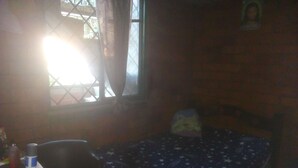 A small room with a single bed, a desk, and a chair. There is a window with curtains, and a picture frame on the wall. - Casa Wilber (Cali)