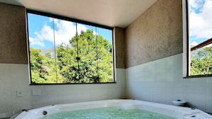 Un jacuzzi rectangular con vistas a un bosque a través de un ventanal grande.
