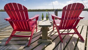 Twee rode Adirondack stoelen gericht op een houten steiger boven water, met een heldere lucht.
