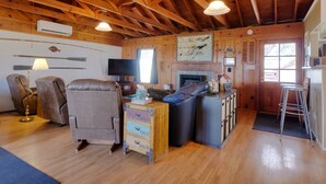 Een gezellig interieur van een chalet met houten plafond, een open haard, een televisie en een eethoek met krukken.