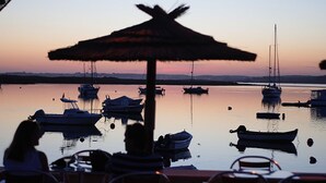 A marina with boats docked at sunset. There are chairs and a table under a thatched umbrella. - Sunset at Vila da Praia - Neat to Alvor Beach and Very Close to Alvor Village (Alvor)