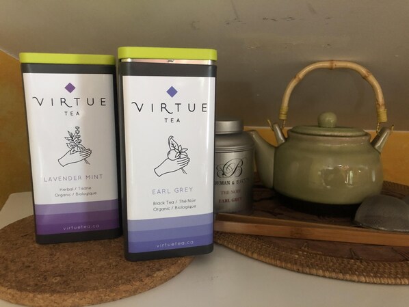 Two Virtue Tea boxes, one labeled Lavender Mint and the other Earl Grey, alongside a teapot and a bottle on a wooden tray.