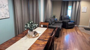 Un comedor con una mesa de madera, sillas, un florero con plantas y un sofá con una silla al fondo.