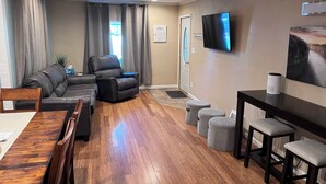 Una sala de estar moderna con un sofá seccional, un sillón reclinable, una mesa de comedor con sillas y un televisor de pantalla plana montado en la pared.
