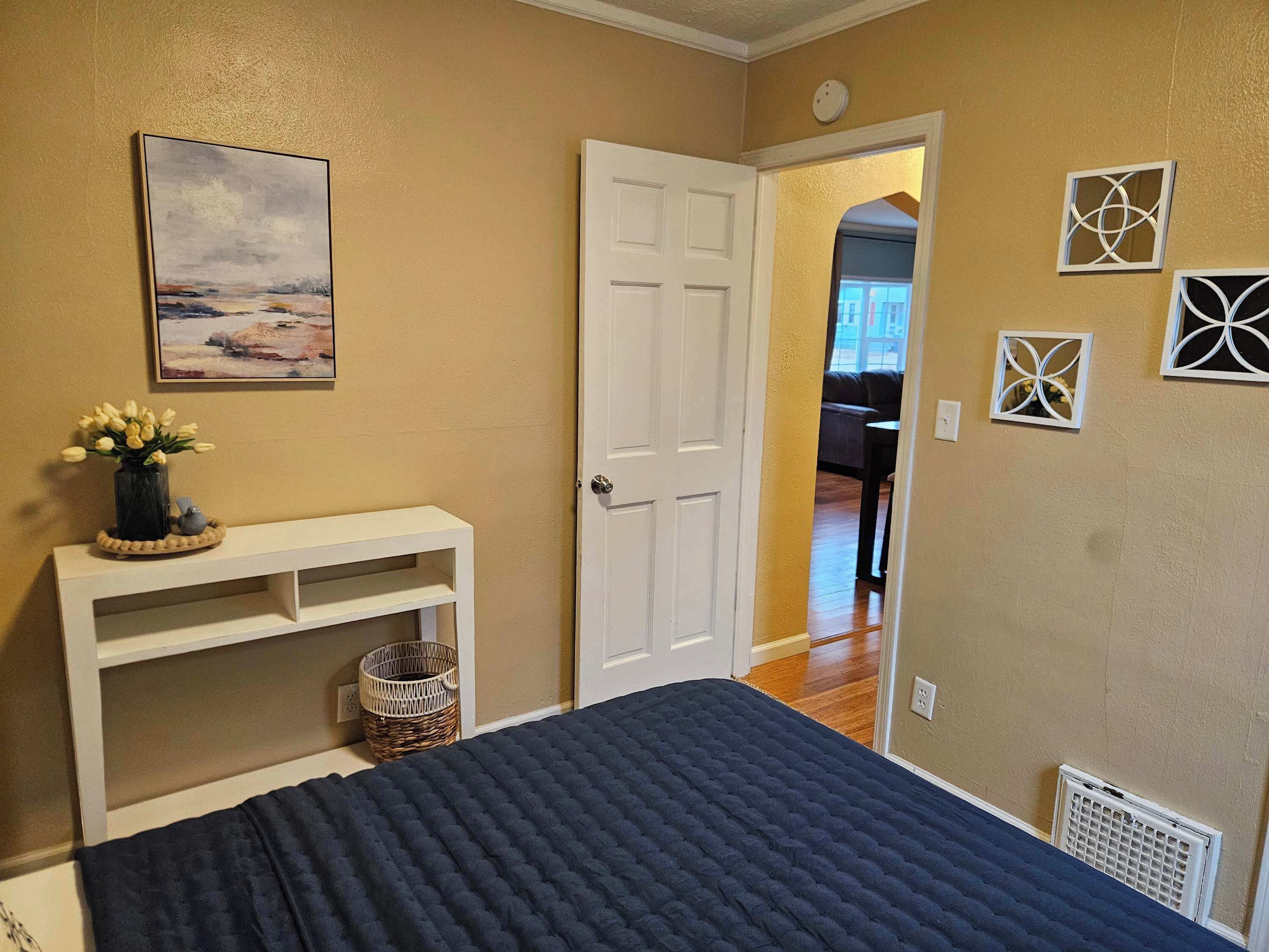 A bedroom with a bed, a white door, a painting, and wall decorations.