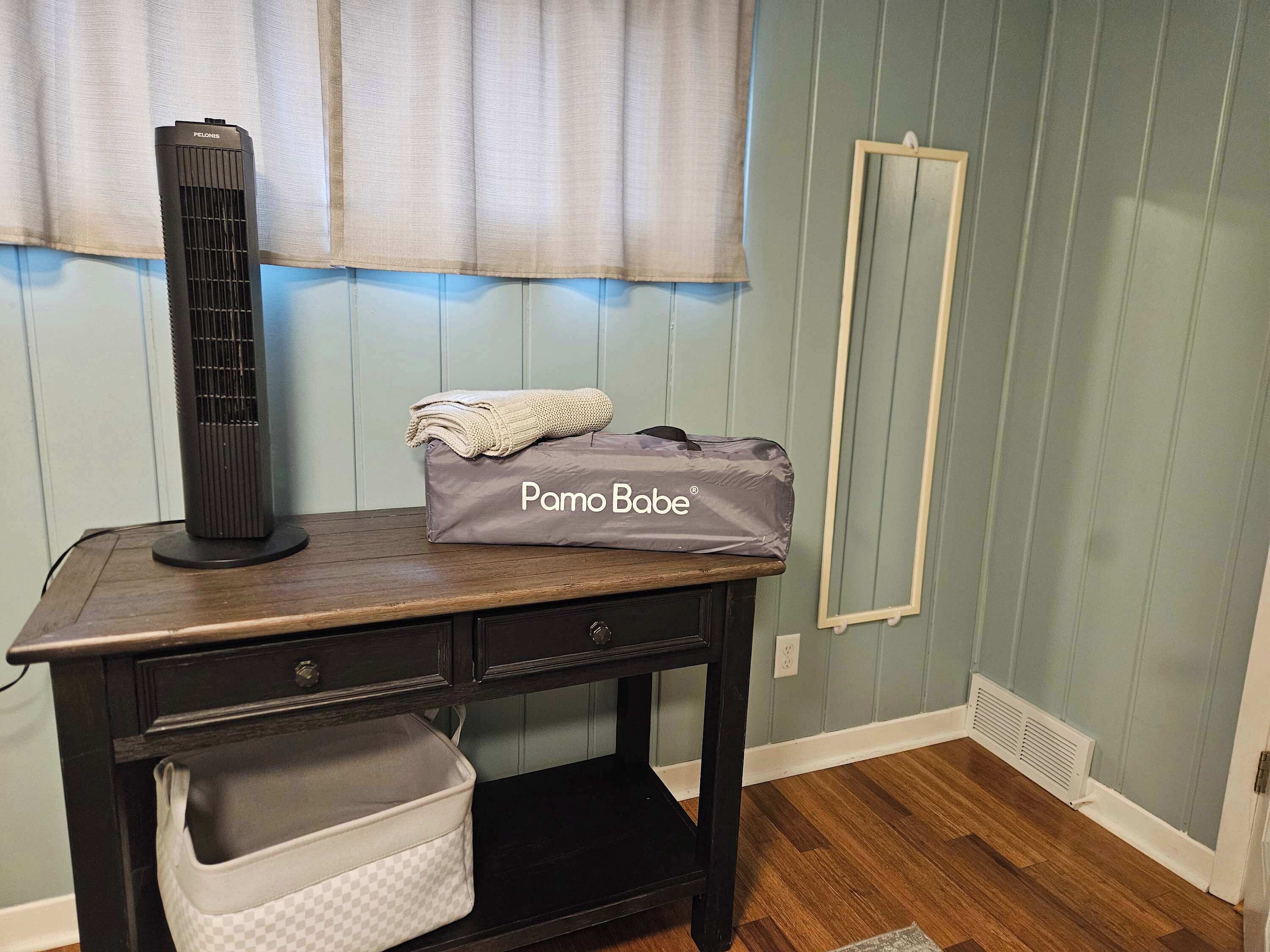 A room with a wooden desk, a black heater, a Pamo Bobe bag, a checkered storage bin, and a radiator.