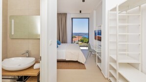 Ein modernes Hotelzimmer mit einem großen Bett, einem Badezimmer mit Waschbecken und Spiegel sowie Blick auf die Stadt durch das Fenster.