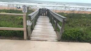 Une promenade en bois mène à une plage où un panneau interdit l’utilisation de récipients en verre sur la plage ou dans l’espace réservé à la piscine.