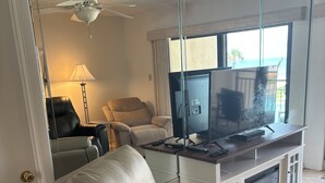 Un salon moderne avec un fauteuil en cuir, une cloison en verre, un ventilateur de plafond, un téléviseur à écran plat et une vue sur l’extérieur.