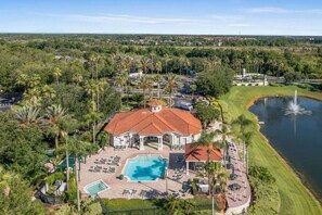 Une grande maison avec une piscine, entourée de palmiers et bordée d’un lac.