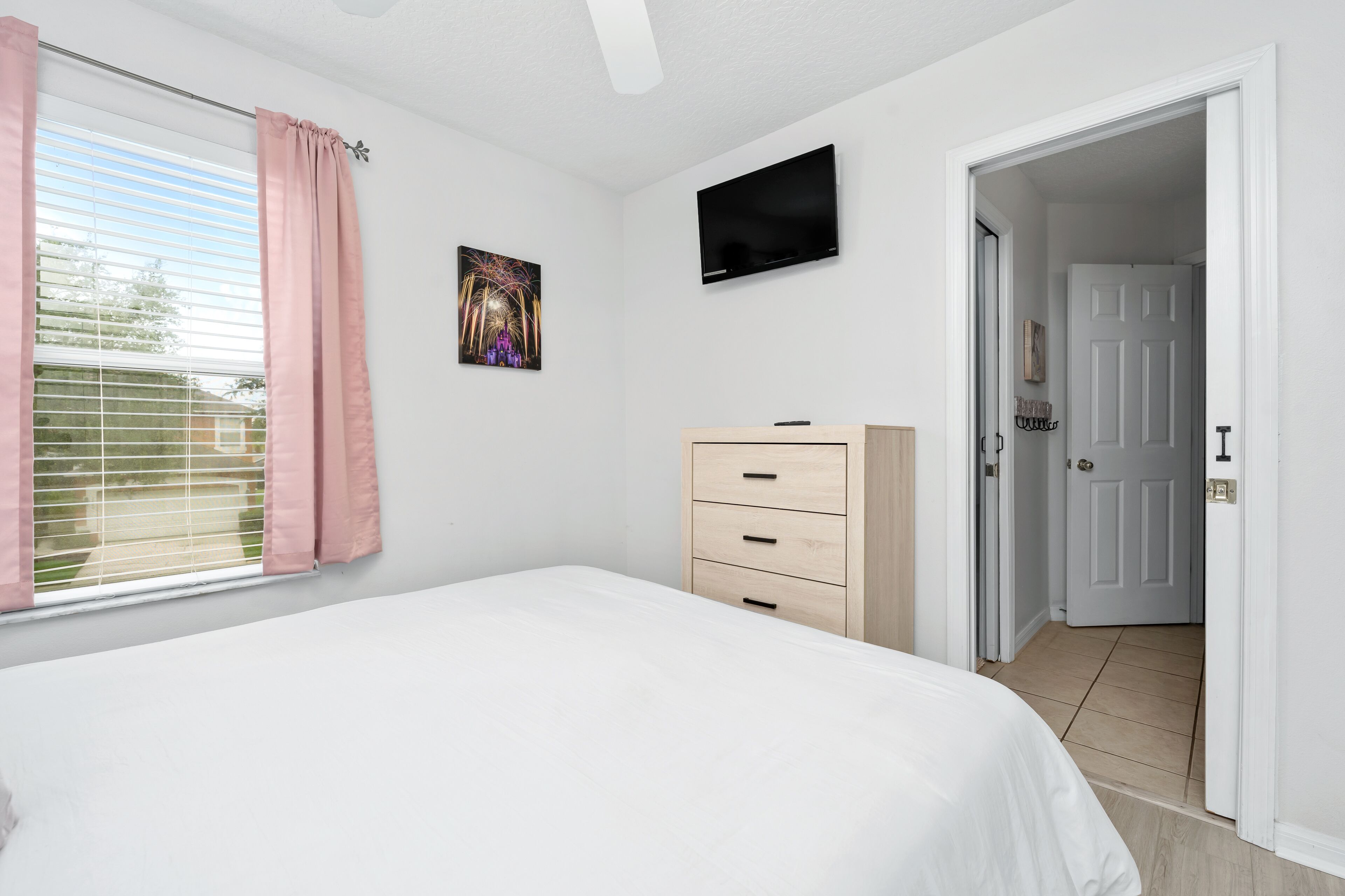 Un dormitorio con cama, televisor, cómoda y una puerta que da a otra habitación.
