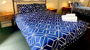 A hotel room with a bed featuring a geometric patterned bedspread, a nightstand with a lamp, a drawer, and a bedside table with a lamp. - Prime Location | North Adelaide 2BR Apt, Melbourne St | Courtyard |Near CBD Events + Private Parking (North Adelaide)
