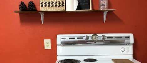 A kitchen with a white stove, a wooden bench, and a red wall.