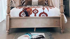 A four-poster bed with a patterned bedspread, a hanging light fixture, and a rug on the floor.