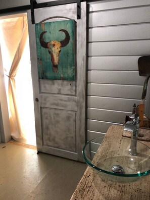 A rustic interior with a door featuring a cow skull artwork, a glass sink, and a wooden countertop.