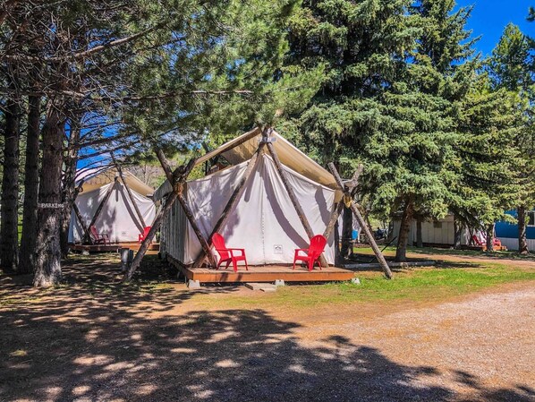 A campsite with two tents, each with a platform and red chairs.