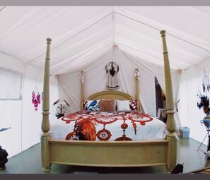 A four-poster bed with a canopy, a wall with dreamcatchers, and a mirror reflecting part of the room.