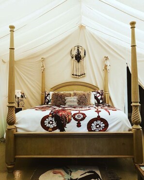 A four-poster bed with a white canopy tent, a patterned bedspread, and a wall-mounted decorative item.
