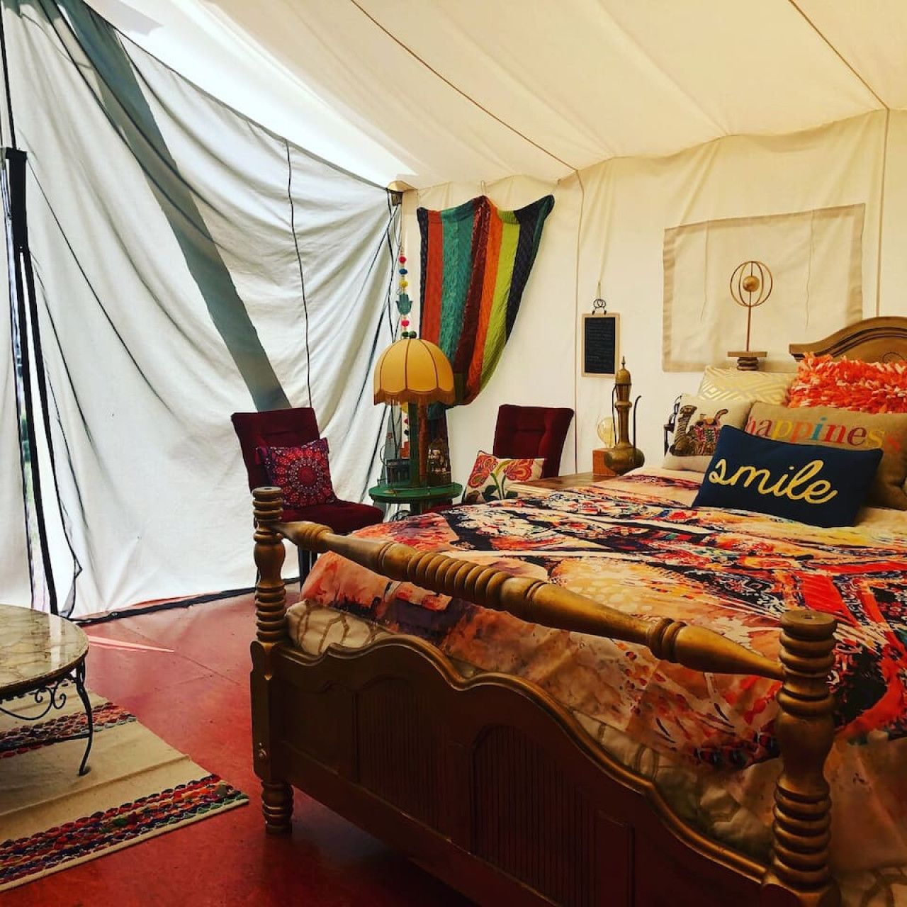 Una habitación con tienda de campaña, una cama de madera, una mesita y una lámpara.
