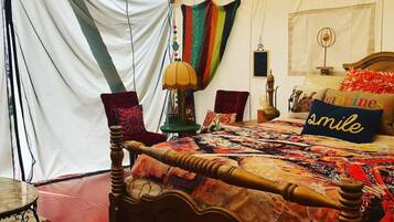 Una habitación con tienda de campaña, una cama de madera, una mesita y una lámpara.