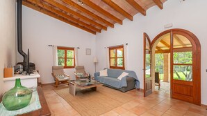 Ein geräumiges Wohnzimmer mit hoher Decke, Holzbalken, einem Kamin, einer Couch, einem Couchtisch und Blick durch einen Rundbogen.