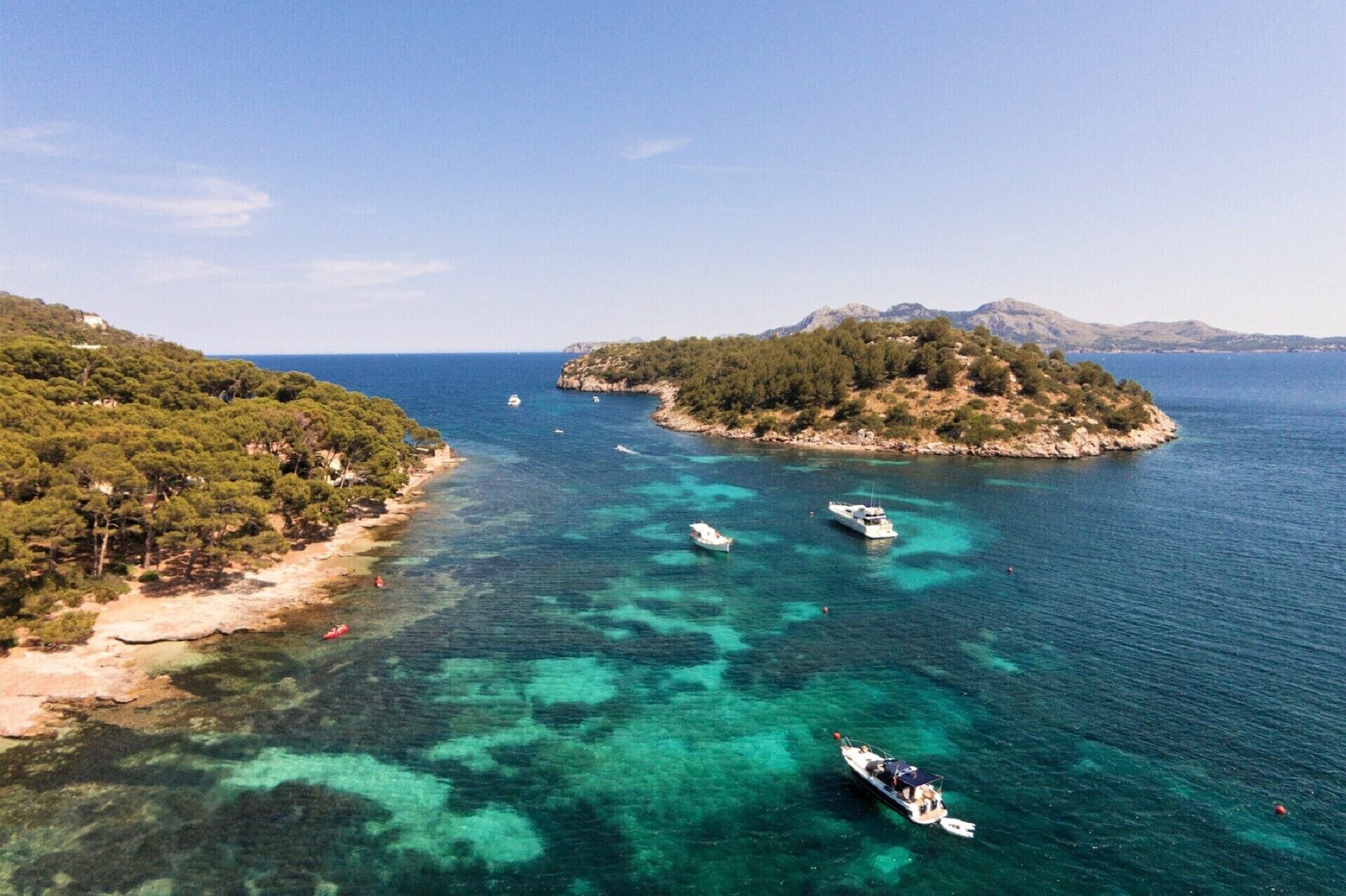 A coastal landscape with clear turquoise waters, boats, and a small island with dense vegetation.