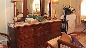 A traditional wooden dresser with a mirror, two lamps, and a vase of flowers. - Port City Guest House (Wilmington)