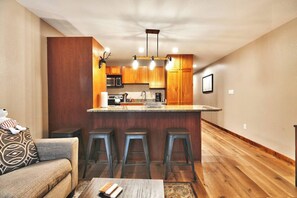 A compact kitchen with a central island, wooden cabinets, and a modern light fixture. - Mountain Views! Hot Tub/Pool Walk to Lifts & Main1 (Park City)