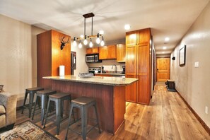 A kitchen with wooden cabinets, a central island with stools, and a ceiling light fixture. - Mountain Views! Hot Tub/Pool Walk to Lifts & Main1 (Park City)