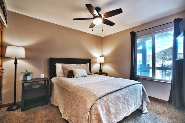A hotel room with a bed, bedside lamps, a ceiling fan, a window with a view, and a small table with a plant. - Mountain Views! Hot Tub/Pool Walk to Lifts & Main1 (Park City)