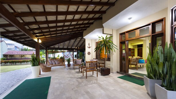 A covered outdoor seating area with wooden furniture and potted plants. - Coqueiros Praia Hotel - Balneário de Iriri (Anchieta)