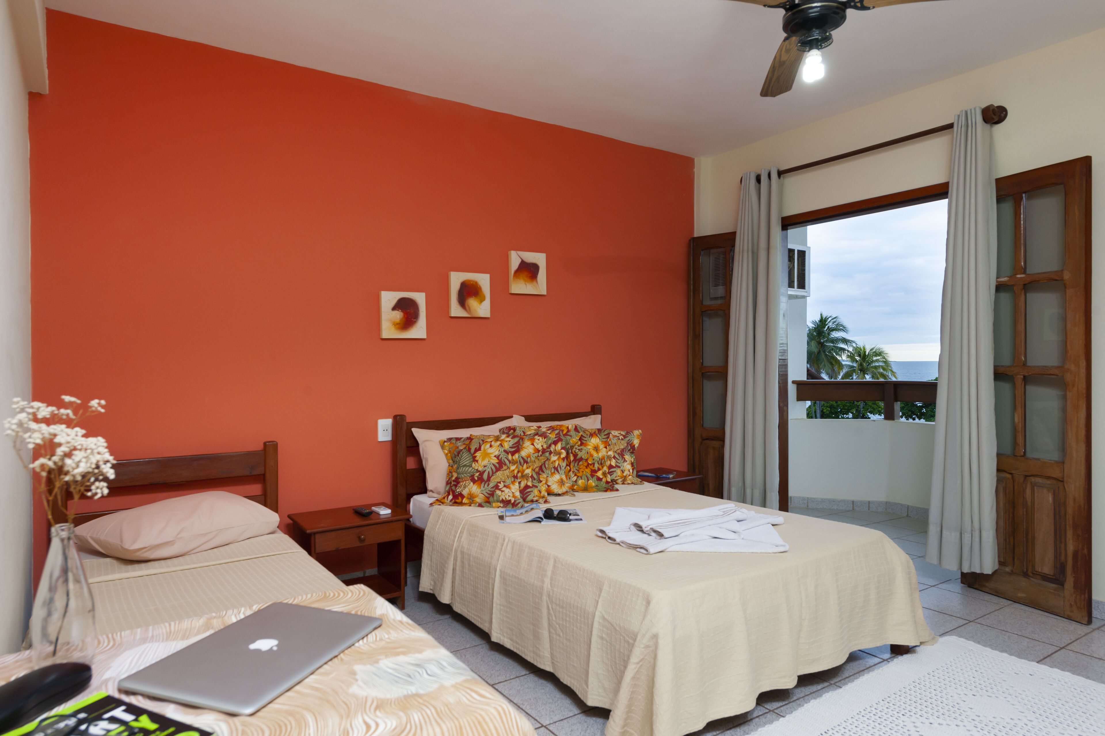 Quarto com duas camas, um laptop em uma delas e vista para o exterior através de uma porta de varanda.