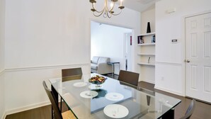 Een eetgedeelte met een glazen tafel, stoelen, een kroonluchter en een witte deur.