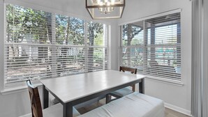 A dining area with a table and chairs, large windows with blinds, and a hanging light fixture. - Hidden Dunes Cottages 2-Bedrooms (Miramar Beach)