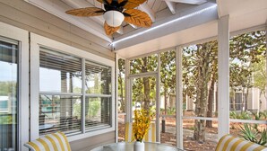 A covered patio with a round glass table, striped yellow and white chairs, and a ceiling fan. - Hidden Dunes Cottages 2-Bedrooms (Miramar Beach)